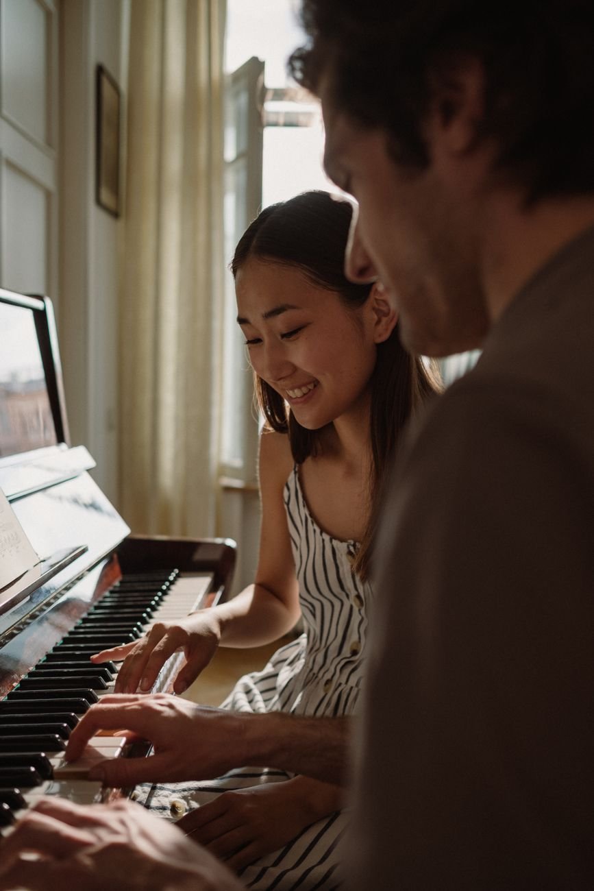 A joyful couple playing the piano together in a sunlit room, highlighting musical connection.