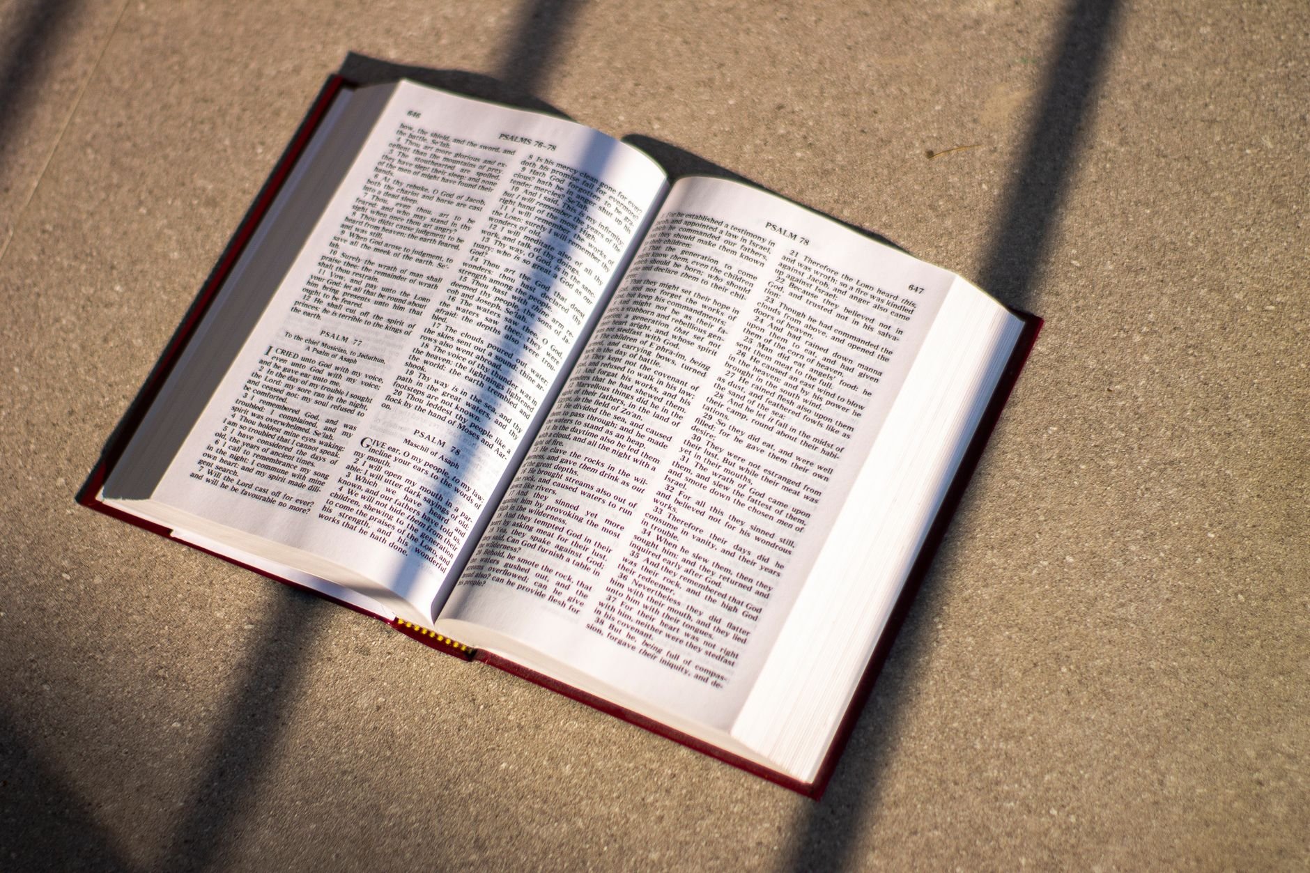An open Bible casting shadows on a floor in natural light, emphasizing scripture and reflection.