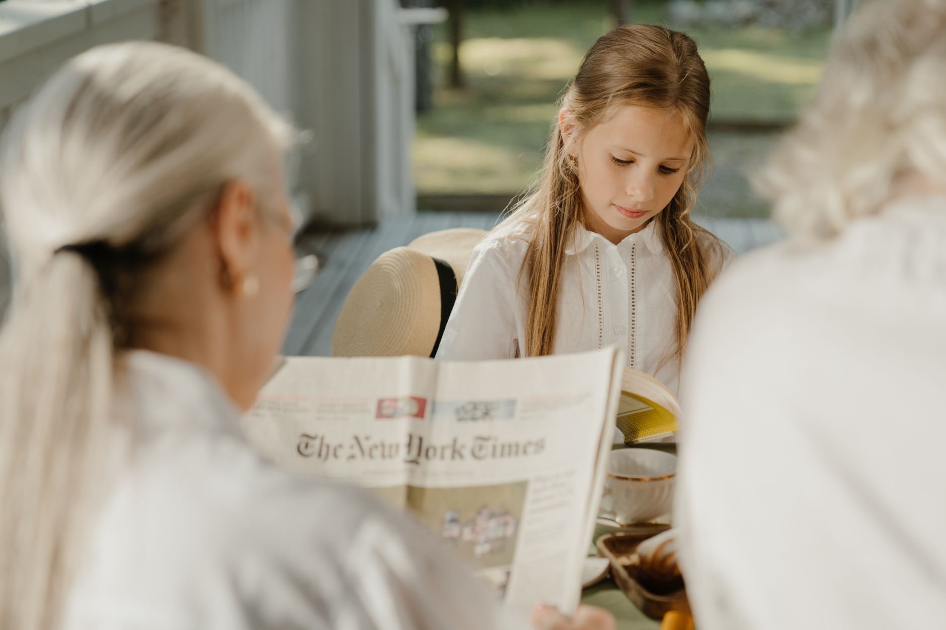 A serene scene of a grandmother and granddaughter reading together on a sunny porch.
